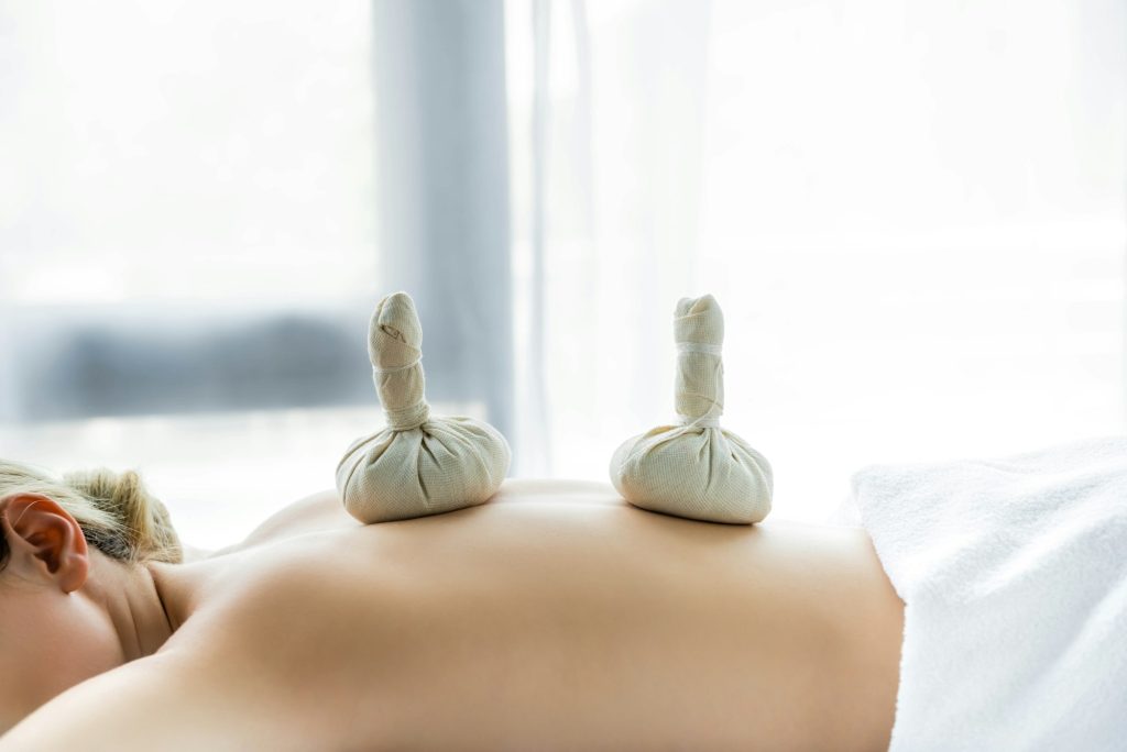 woman lying on massage mat with herbal balls on back